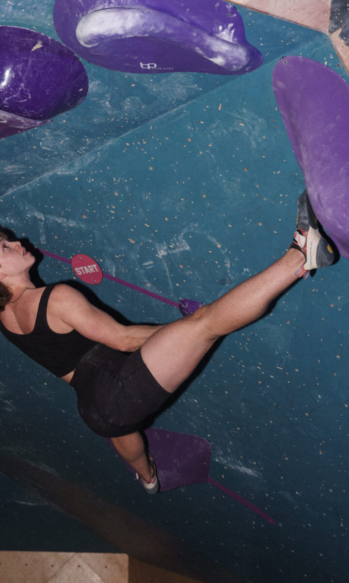 A person in athletic gear climbs an indoor bouldering wall at Eckington, stretching her left leg high and reaching up with determination—focused and strong for the Partners Page.