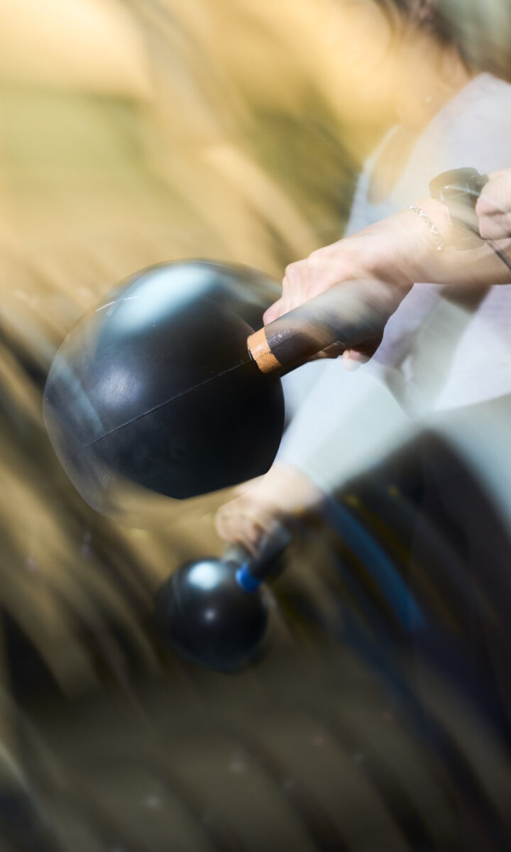 A person swings a black kettlebell, captured in motion blur—perfect inspiration for your Fitness Calendar. Their hand firmly grips the handle, and their forearm and wrist are visible, with a blurred background suggesting movement.