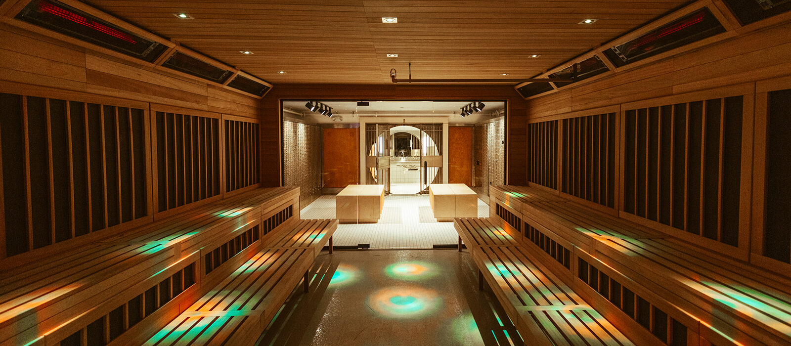 A spacious modern sauna at the climbing gym in Seattle’s University District features wooden benches, warm lighting, and colorful circular light patterns on the floor, leading to a glass door opening to a well-lit relaxation area.