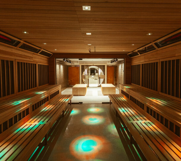 A spacious modern sauna at the climbing gym in Seattle’s University District features wooden benches, warm lighting, and colorful circular light patterns on the floor, leading to a glass door opening to a well-lit relaxation area.