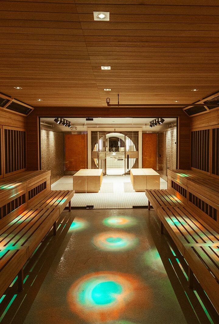 A spacious modern sauna at the climbing gym in Seattle’s University District features wooden benches, warm lighting, and colorful circular light patterns on the floor, leading to a glass door opening to a well-lit relaxation area.