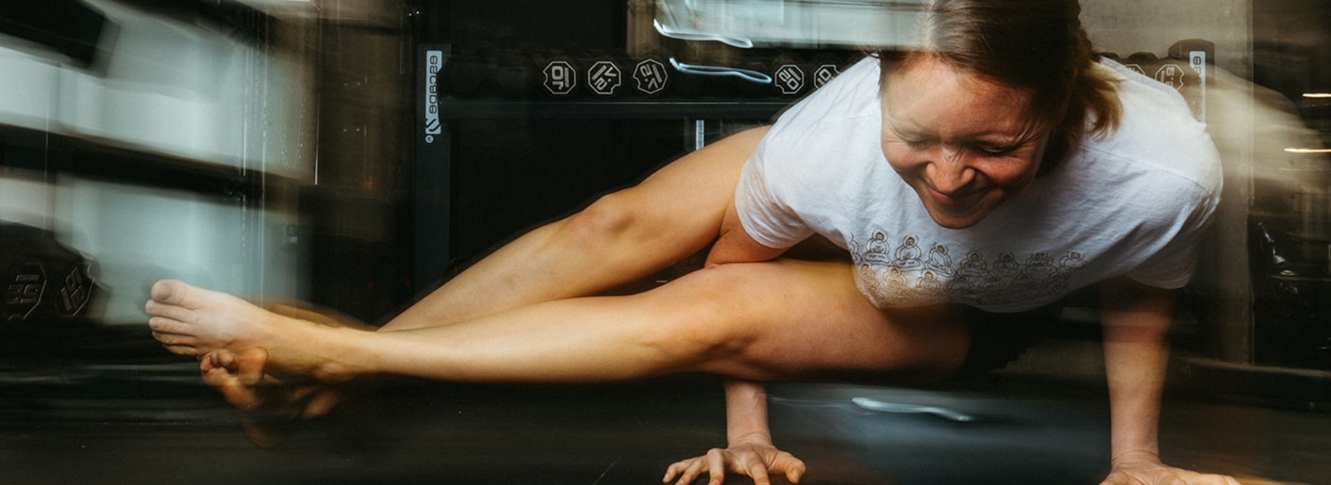 A woman balances on her hands in a challenging yoga pose at the gym, smiling and extending her legs to the side. Motion blur emphasizes strength and movement—perfect for showcasing membership benefits or special pricing offers.