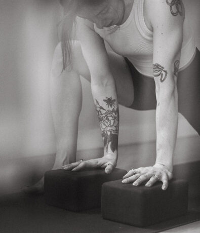 A person with tattoos practices yoga in a climbing gym in Seattles University District, leaning forward with both hands pressing on yoga blocks and one knee bent. The black and white image highlights the focus and strength in the pose.