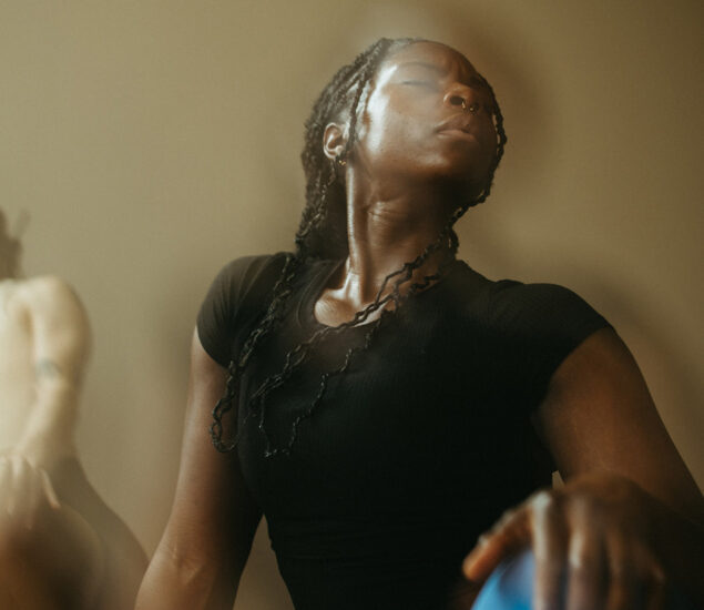 A person with braided hair and a nose ring, wearing a black top, leans back with eyes closed in a relaxed pose. The soft, warm lighting creates a dreamy atmosphere reminiscent of carefree summer membership moments.