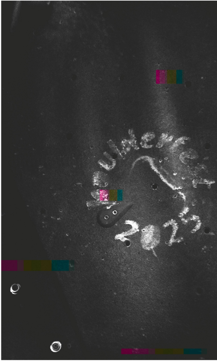 A dark, grainy surface with the handwritten white chalk text Remember 2023 encircled and an arrow drawn below, reminiscent of notes from the Austin Boulderfest competition. Colored rectangular artifacts and a few small round holes mark the scene.