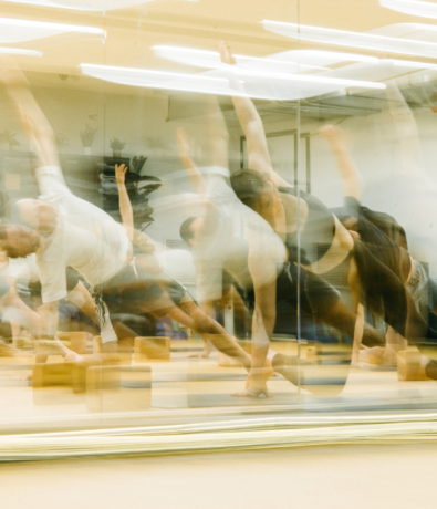 A group of people performing side plank yoga poses in a studio with mirrored walls; the image has a motion blur effect, creating overlapping shapes and dynamic movement, reminiscent of climbing fluidly through space.