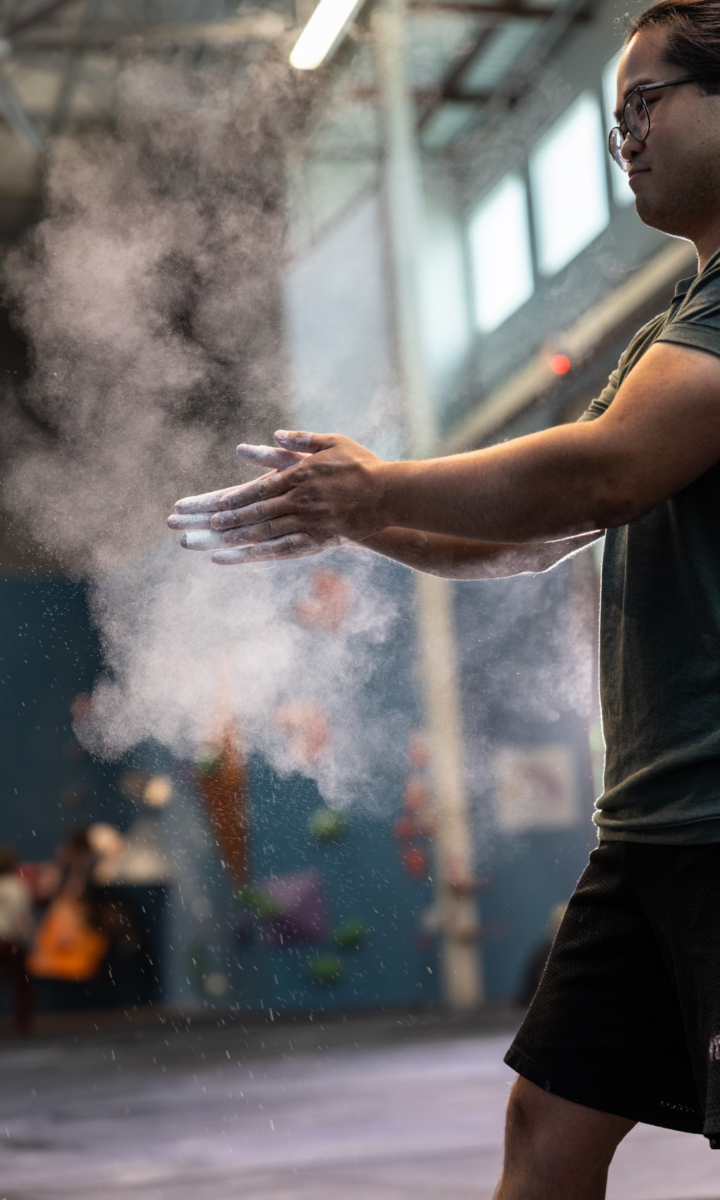 A person claps their chalk-covered hands, creating a cloud of chalk dust in an indoor gym with climbing walls—and K&N air filters in gyms help keep the air cleaner for everyone.