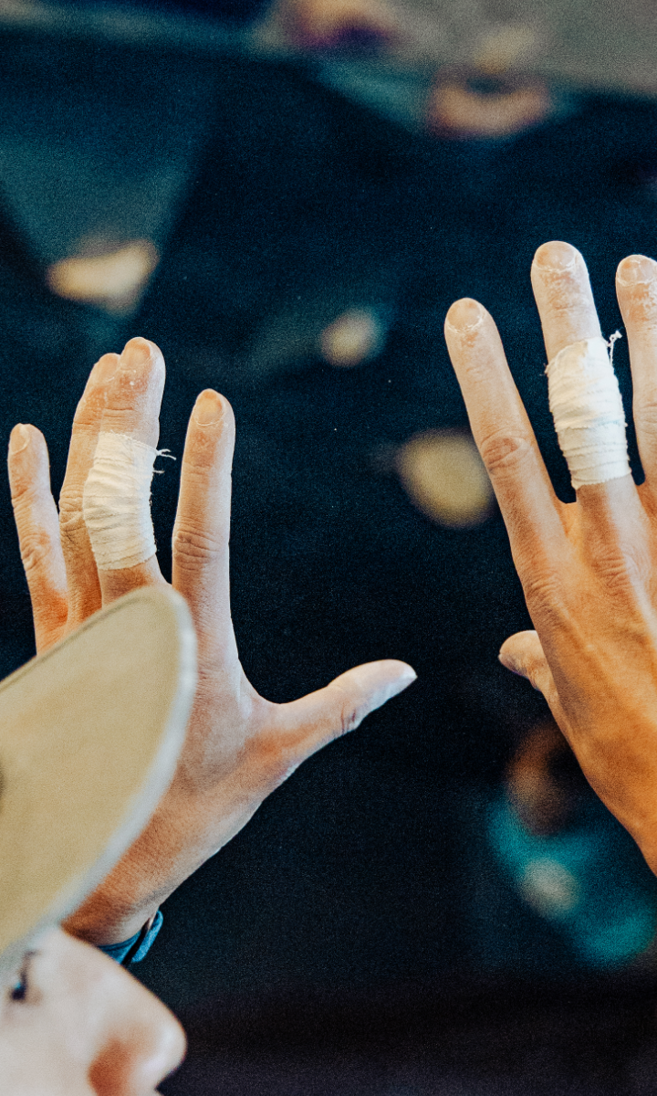 Close-up of two hands with chalk and fingers wrapped in athletic tape, likely preparing for rock climbing or gymnastics private instruction, with a blurred background.
