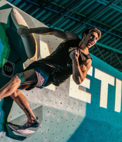 A climber in athletic wear grips an indoor climbing wall in Minneapolis, muscles tense and face focused, as they reach for the next hold under bright, dramatic lighting—perfect for Private Coaching sessions.