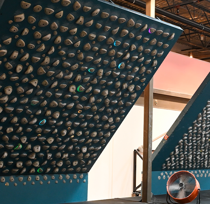 Two steeply angled Training Boards covered with numerous gray holds stand side by side in a modern climbing gym at Westgate, featuring industrial design elements and metal railings.